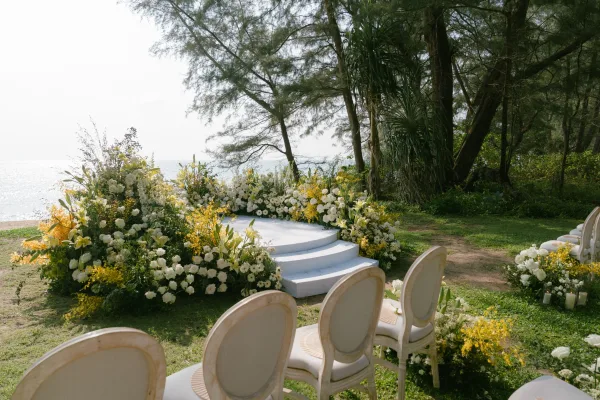 Outdoor ceremony setup for a beach wedding ceremony overlooking the ocean, featuring an aisle lined with candles on a grassy lawn under open sky