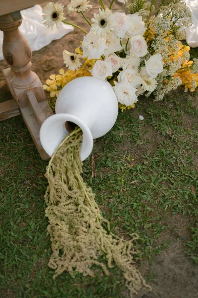Wedding floral arrangement of white and yellow wedding flowers in a white ceramic urn, arranged in an organic, textured garden style.