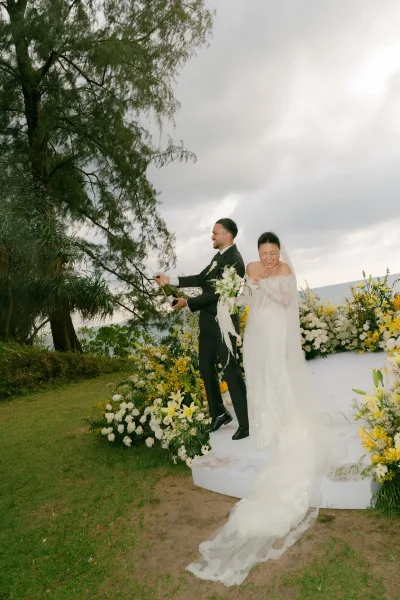 Wedding champagne pop as a jubilant champagne spray surrounds newlyweds on an oceanfront lawn, her cathedral veil trailing behind.
