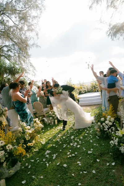 Wedding kiss moment during the ceremony recessional as newlyweds walk the aisle through fluttering flower petals on a sunny garden lawn