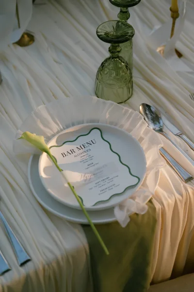 Wedding place setting with green and white table decor, a single calla lily at the plate, set on an ivory tablecloth with elegant simplicity.