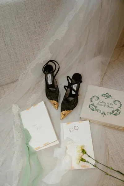 Wedding details flatlay featuring Jimmy Choo bridal heels beside elegant vow books, styled in a modern romantic composition.