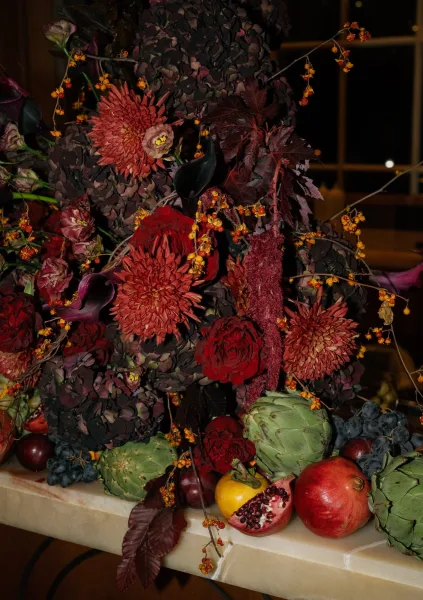Wedding centerpiece in a fall floral arrangement with a pomegranate accent, set on a stone tabletop by window panes in an indoor setting.