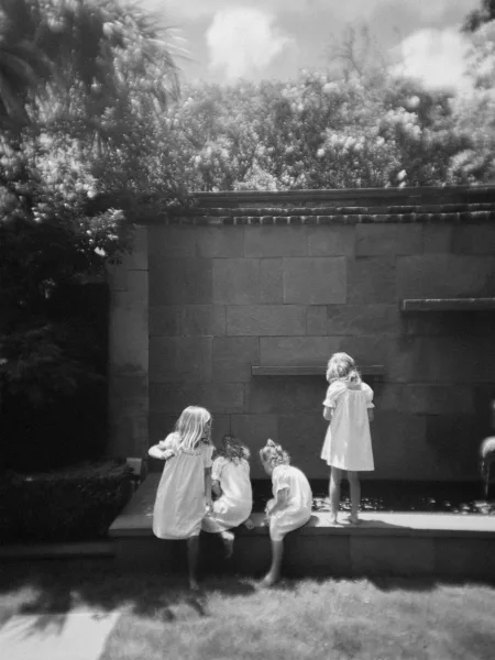 Flower girls moment in black and white as little girls hold hands by a stone fountain in a garden, their simple dresses swaying.