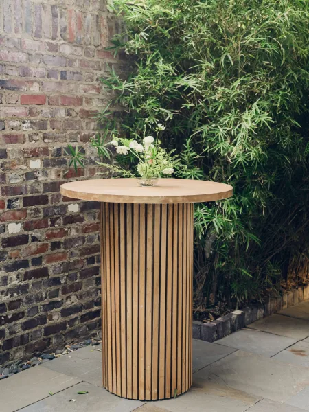 Cocktail table decor with a bud vase centerpiece sits on a stone patio before a brick wall and bamboo plants.