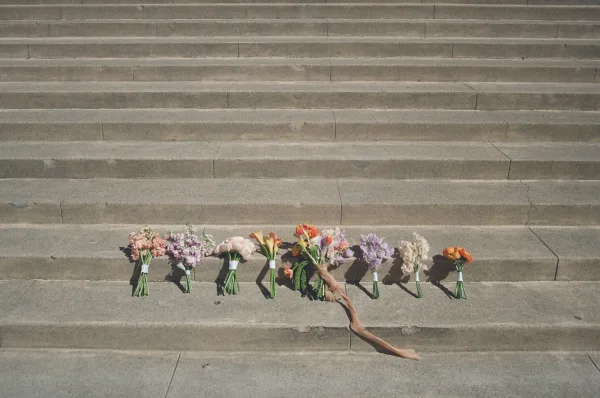 Bridal bouquets arranged in a bridesmaid bouquet lineup on sunlit stone steps, each mixed flower bouquet finished with silk ribbon streamers