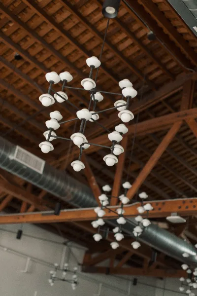 Wedding reception lighting with a modern chandelier of globe bulbs and black metal arms beneath a wood beam ceiling with exposed ductwork