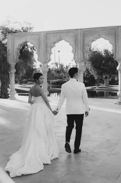Couple portrait in a black and white wedding photo, holding hands by a reflecting pool with ornate archways on a stone terrace backdrop