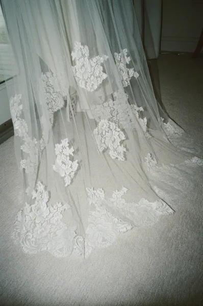 Lace wedding veil with cathedral veil lace appliques spread over a bridal gown train, scalloped edge draping on a carpeted floor indoors