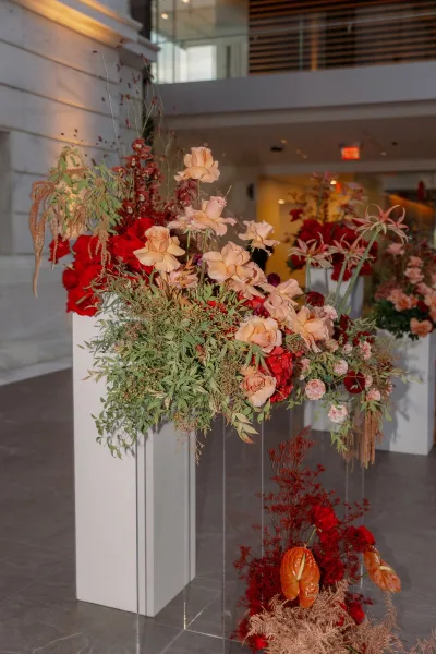 Wedding floral installation with ceremony floral columns of red and blush roses on acrylic pedestals in a modern indoor hallway with stone wall