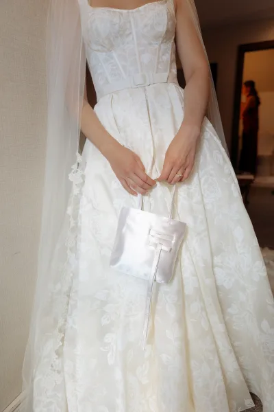 Wedding dress close-up showing a strapless wedding dress with floral jacquard fabric, satin belt, tulle veil, and ring indoors