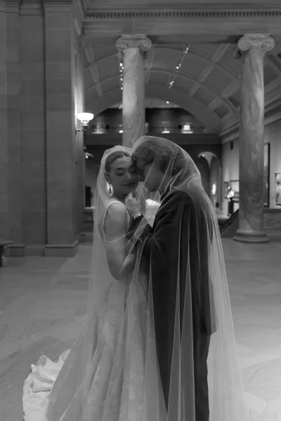 Wedding couple portrait of bride and groom under veil, forehead touch in a grand museum hall with marble columns and arched ceiling