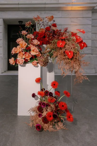 Wedding floral arrangement with ceremony entrance flowers on white and clear pedestals, red anthurium and roses by a stone doorway