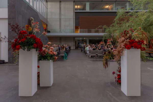 Ceremony aisle design with floral arrangements on white plinths and pampas grass, set in a modern atrium with concrete walls and glass railings
