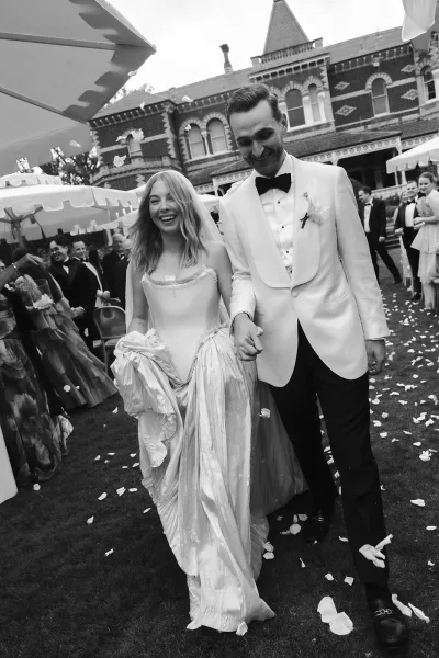Wedding recessional as bride and groom walk down the aisle through a rose petal toss, veil flying, guests by a historic brick building