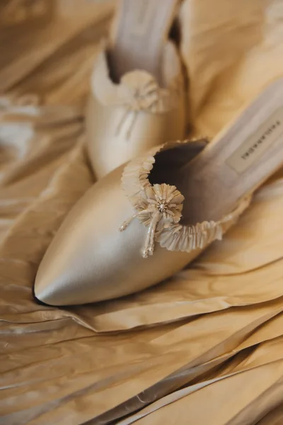 Bridal shoes in ivory wedding heels, satin pointed-toe pumps with rosette embellishments and beaded detail on draped fabric