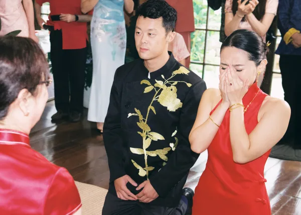Ceremony moment at a tea ceremony wedding, couple kneeling as bride in red cheongsam cries while guests watch near bright windows
