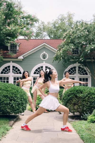 Bridal party photo of bridesmaids group photo in matching crop tops and tennis skirts, smiling on a garden path by an arched-window house