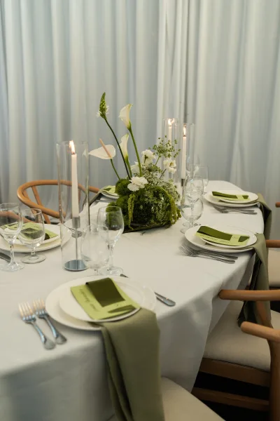 Reception tablescape with wedding table centerpiece of green and white calla lilies, tall taper candles, and place cards against white drapes