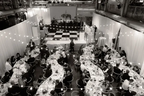 Wedding reception decor in an industrial wedding reception with string lights and white draping over long banquet tables and a checkered dance floor