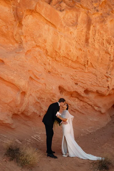 Wedding kiss portrait of bride and groom kissing by a sandstone rock wall, bride in tulle veil and gloves with a small bouquet