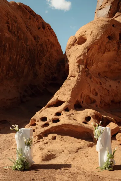 Ceremony setup with outdoor ceremony backdrop, white draping on pedestals and calla lilies set before red rock canyon cliffs