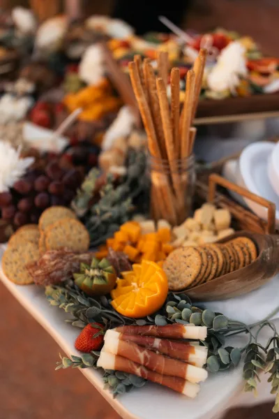 Charcuterie board with wedding cocktail hour food, featuring cheeses, cured meats, grapes and citrus on rustic wood board on white tablecloth