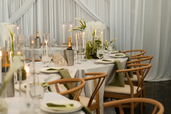 Reception tablescape wedding table setting with calla lilies, greenery, taper and glass cylinder candles on white linens in a draped tent