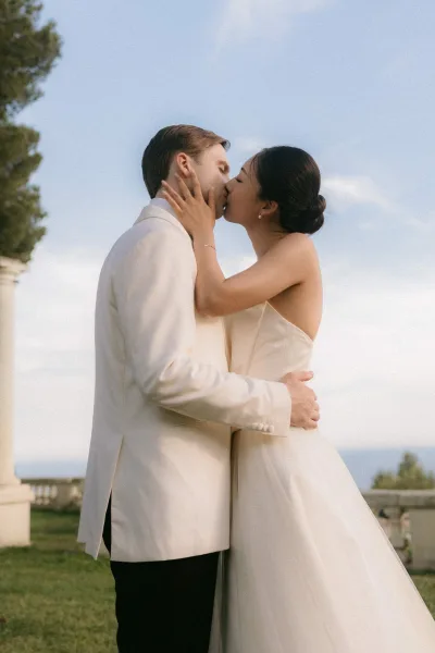 Wedding kiss portrait, a tender couple portrait of the bride and groom embracing; her stud earrings glint as they kiss by a stone balustrade.