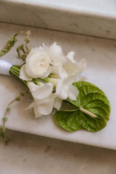 Bridal bouquet, a white calla lily bouquet with a satin ribbon wrap, rests on a cool marble step against a stone surface.