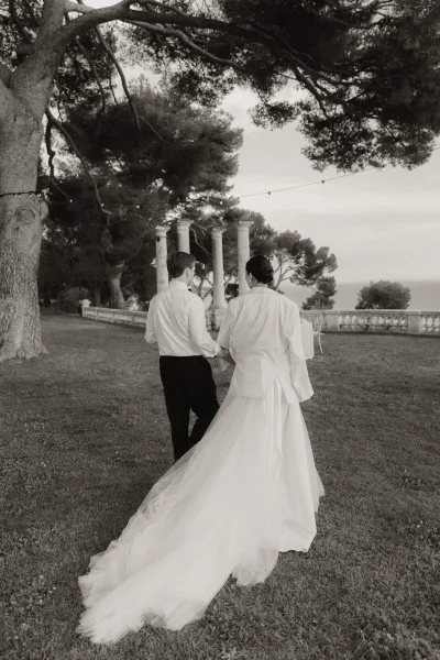 Couple portrait of a garden bride and groom on a lawn by stone balustrade and columns, her tulle train sweeping toward an ocean view.