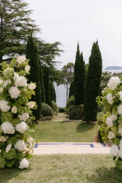 Ceremony aisle design framed by floral pillars along an outdoor ceremony aisle amid cypress trees on a garden lawn overlooking the ocean.