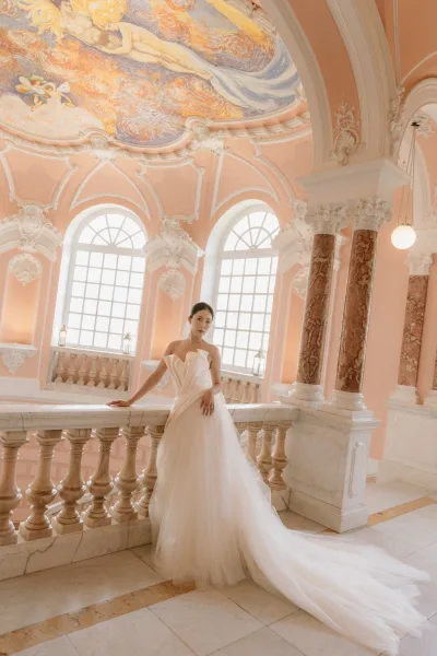 Bridal portrait of a bride in strapless gown with a tulle train, posed by marble columns and arched windows in a grand hall