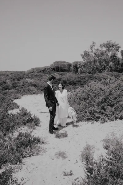 Couple portrait in a black and white wedding portrait holding hands on sand dunes, bride in gown with veil and bouquet, groom in suit