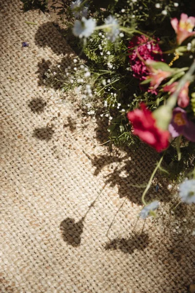 Wedding bouquet with wildflower bridal bouquet blooms, baby's breath accent, and greenery resting on a woven rug in sunlight shadows
