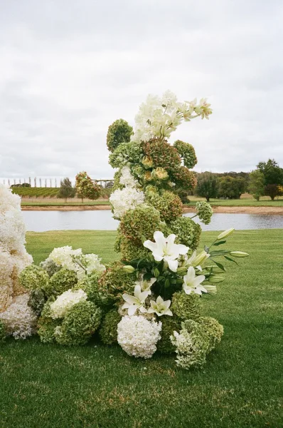 Ceremony flowers styled as lush outdoor ceremony florals with hydrangeas by a lakeside vineyard under a cloudy sky.