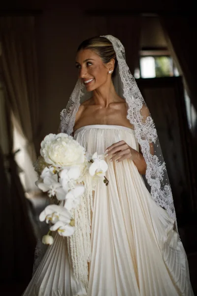 Bridal portrait of a bride with bouquet, holding white orchids, posed near a mirror and draped curtains.