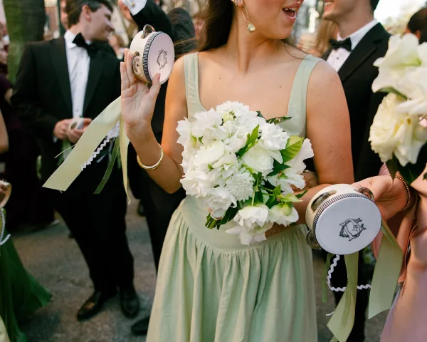 Bridesmaid moment with a bridesmaid holding bouquet, laughing in a mint dress with ribbon streamers as guests line a tree-lined walkway