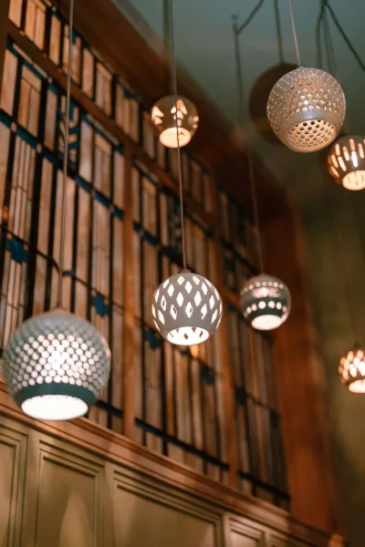 Pendant lighting for indoor wedding lighting, featuring perforated shades that cast warm patterns against wood paneling and a metal grid backdrop.