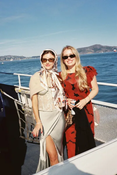 Wedding guests portrait highlighting stylish wedding guest outfit choices, with a headscarf accent, on a boat deck against ocean and mountains.