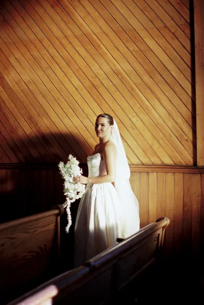 Bridal portrait of a bride holding bouquet in a strapless satin ball gown, her cascading bouquet framed by wooden pews.