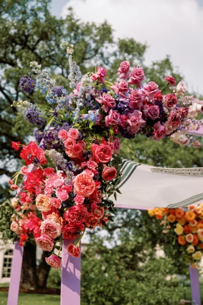 Wedding floral arch with ceremony arch flowers in pink and purple blooms, lush greenery, and draped fabric on a painted wood frame in a garden lawn setting
