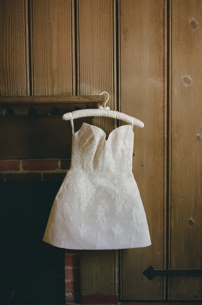Wedding dress close-up of a lace wedding dress with a sweetheart neckline, set against a wood-paneled wall and brick fireplace mantel.