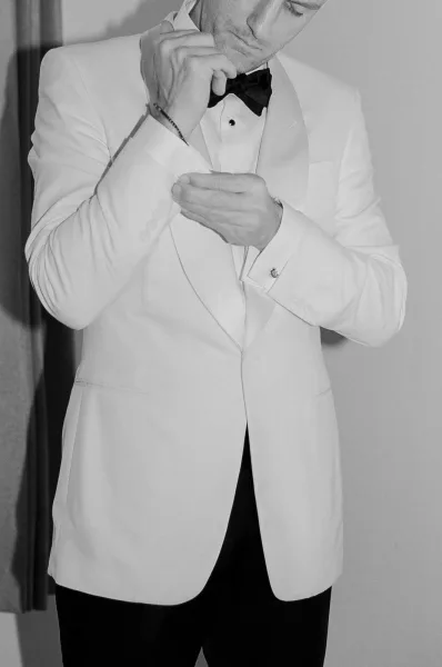 Groom getting ready in black tie groom style, adjusting cufflinks with steady hands, calm focus before the ceremony.