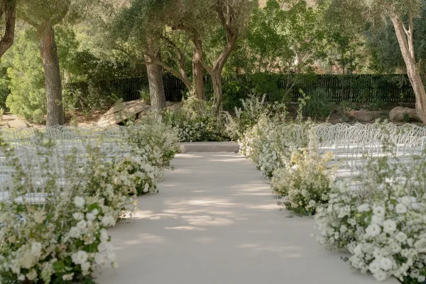Ceremony aisle design for an outdoor ceremony setup with an aisle runner, set amid trees, garden shrubs, rocks, and a wooden fence.