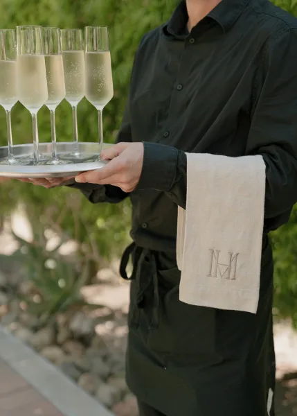 Champagne service with tray passed champagne presented on embroidered linen, set against garden greenery and a stone border walkway.