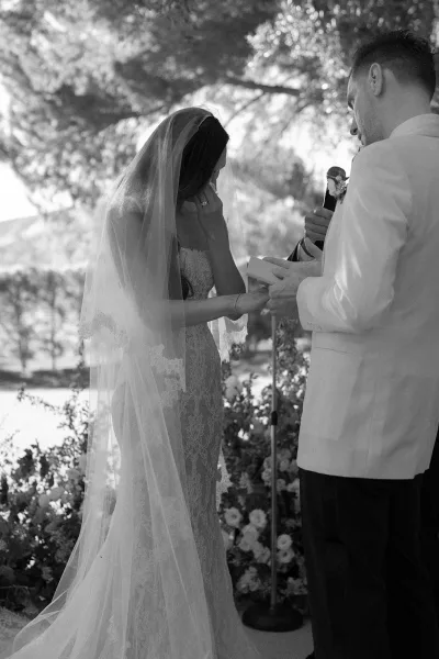 Wedding vows in an outdoor ceremony moment as the couple stands with a vow book amid sunlit garden trees and hedges.