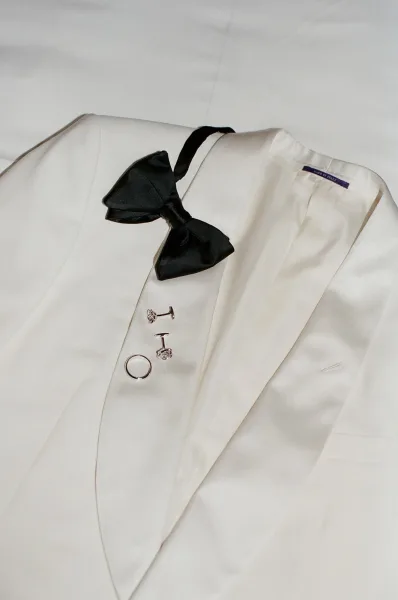 Groom accessories with a black bow tie arranged on white fabric, a simple composition emphasizing classic, formal wedding style.