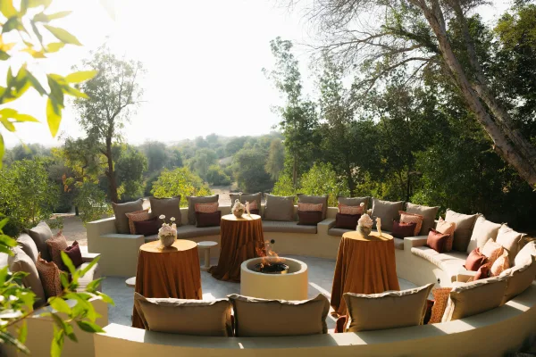 Wedding lounge area with outdoor wedding lounge sectional seating, throw pillows, cocktail tables, and candles around a fire pit on a patio with hillside view