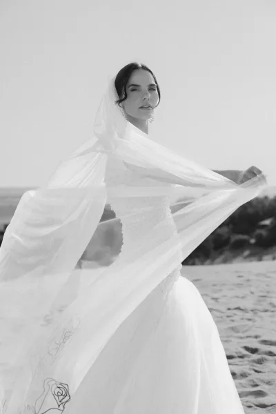 Bridal portrait in black and white of a bride in a strapless dress with veil over her face, drop earrings, and sand dunes behind